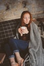 Young sick woman healing with hot drink at home on cozy couch