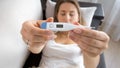 Young sick woman lying on sofa and showing digital thermometer display in camera Royalty Free Stock Photo