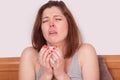 Young sick woman with red nose sitting in bed and sneezing.