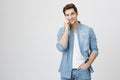 Young sincere male smiles to camera while talking on phone with one hand in pocket, isolated over white background Royalty Free Stock Photo