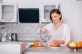 Young sincerely smiling female pouring a purified mineral water into transparent glass decanter at modern kitchen. Plenty of