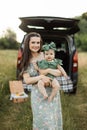 Young single mother holding on hands her little daughte,r standing on the grass during a picnic