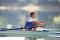 A Young single scull rowing competitor paddles on the tranquil lake