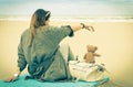 Young single woman sitting at the beach with her teddy bear