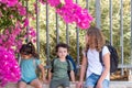 Little girls with blonde hair and black hair and toddler brother with curly hair sitting near a closed metallic fence. Royalty Free Stock Photo