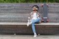 Young skateboarder girl chilling listen to music closed eyes on bench on urban park near longboard Royalty Free Stock Photo