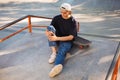 Young skater in cap holding his painful leg with skateboard near while spending time at skatepark Royalty Free Stock Photo