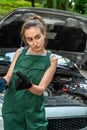 young skilled specialist mechanic woman in overalls and tools in hands near broken car.