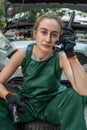 young skilled specialist mechanic woman in overalls and tools in hands near broken car.