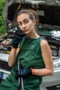 young skilled specialist mechanic woman in overalls and tools in hands near broken car.