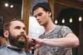 Young skillful barber making haircut to handsome bearded man