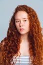 Young skin care concept. Beautiful red-haired girl with curls on a blue background in the studio without makeup. Royalty Free Stock Photo