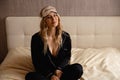 Young Sleeping Beuty blonde woman wearing blindfold sleep mask sitting on her bedroom bed going to bed - Wearing black Royalty Free Stock Photo