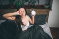 Young sleeping woman and alarm clock in bedroom at home. Girl overslept in bed and looking alarm clock in shock Royalty Free Stock Photo