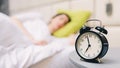 Young sleeping woman and alarm clock in bedroom at home - shallow depth of field Royalty Free Stock Photo