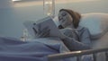 Young sleepless patient lying in the hospital bed and reading a book