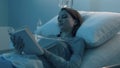 Young sleepless patient lying in the hospital bed and reading a book