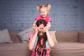 A young slender beautiful mother with her blond daughter on her shoulders play, enjoy and indulge in the teams near the sofa on th Royalty Free Stock Photo