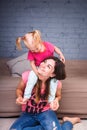 A young slender beautiful mother with her blond daughter on her shoulders play, enjoy and indulge in the teams near the sofa on th Royalty Free Stock Photo