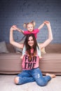 A young slender beautiful mother with her blond daughter on her shoulders play, enjoy and indulge in the teams near the sofa on th Royalty Free Stock Photo