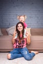 A young slender beautiful mother with her blond daughter on her shoulders play, enjoy and indulge in the teams near the sofa on th Royalty Free Stock Photo