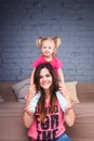 A young slender beautiful mother with her blond daughter on her shoulders play, enjoy and indulge in the teams near the sofa on th Royalty Free Stock Photo