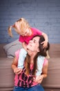 A young slender beautiful mother with her blond daughter on her shoulders play, enjoy and indulge in the teams near the sofa on th Royalty Free Stock Photo