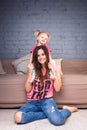 A young slender beautiful mother with her blond daughter on her shoulders play, enjoy and indulge in the teams near the sofa on th Royalty Free Stock Photo