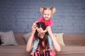 A young slender beautiful mother with her blond daughter on her shoulders play, enjoy and indulge in the teams near the sofa on th Royalty Free Stock Photo