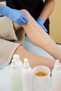 A young slender girl applies sugar paste for hair depilation on her legs. Close-up.