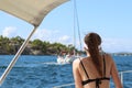 A young slender girl in a swimsuit sits on the stern and watches a sailing yacht passing by. A luxury holiday on the water for wea Royalty Free Stock Photo