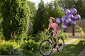 young slender woman, cheerfully rides a bicycle, holding a bunch of purple balloons in her hand