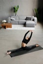 A young slender woman does splits to stretch her legs. Joyful talented woman doing twine in the living room of the house. Healthy