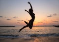 Young slender woman enthusiastically jumps up and has fun at sunset on the beach by the sea