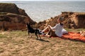 Rear View Of Woman With Dog Sitting On Hill Against Sea At Sunset. Royalty Free Stock Photo