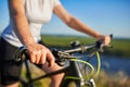 Young slender woman sitting on bicycle, holding handlebars with hands. Woman in the park sunset lighting.
