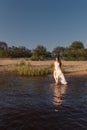 Young slender woman walks out of the beach going into the water holding a wet white summer dress exposing her legs to the knee Royalty Free Stock Photo