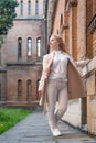 Young slender woman in white clothes near old red brick building looking into the side. Girl alone. Vertical frame Royalty Free Stock Photo