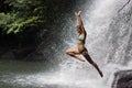 Young athletic woman jumping into water with raised hands. Background of many drops of waterfall and tropical forest Royalty Free Stock Photo