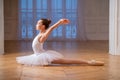 Young slim ballerina in a white tutu is dancing swan on pointe shoes in a spacious bright room