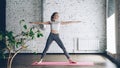 Young slim blond girl is doing yoga complex in studio with white walls. She is starting with warrior poses, then bending Royalty Free Stock Photo