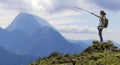 Young slim blond tourist girl with backpack points with stick at foggy mountain range panorama standing on rocky top on bright