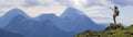 Young slim blond tourist girl with backpack points with stick at foggy mountain range panorama standing on rocky top on bright