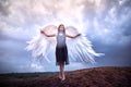 Young slim girl in black dress with with white wings dances on sand dunes against a dramatic sky before a thunderstorm Royalty Free Stock Photo