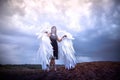 Young slim girl in black dress with with white wings dances on sand dunes against a dramatic sky before a thunderstorm Royalty Free Stock Photo