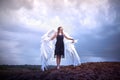 Young slim girl in black dress with with white wings dances on sand dunes against a dramatic sky before a thunderstorm Royalty Free Stock Photo