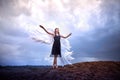 Young slim girl in black dress with with white wings dances on sand dunes against a dramatic sky before a thunderstorm