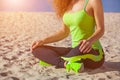 Young slim girl in black and light green tracksuit sitting after a workout in the sand on the seashore. Royalty Free Stock Photo