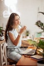 A young slim girl with long hair,wearing casual style, sits at the table with a laptop and looks at her phone in a cozy