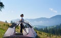 Young woman having a rest near tourist tent in the summer morning in the mountains Royalty Free Stock Photo